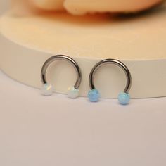 two silver hoop earrings with opal beads on a white surface next to a pink flower