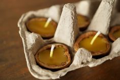 three candles are sitting in an egg carton on a wooden table with wax paper