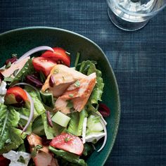 a green bowl filled with salad and meat on top of a table next to utensils