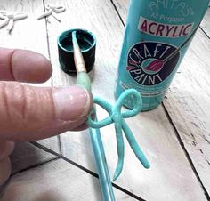 a person is holding an item with scissors and glue on it, next to a tube of acrylic