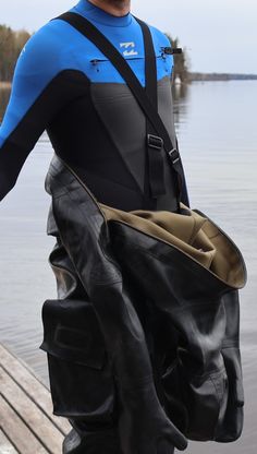 a man in a wet suit carrying a large black bag on a dock next to the water