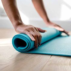 a person rolling up a yoga mat on the floor with their hand and thumb resting on it