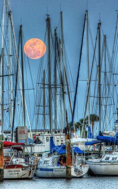 the full moon is setting over sailboats docked