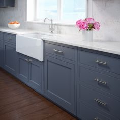 a white sink sitting under a window next to a bowl of fruit on top of a counter