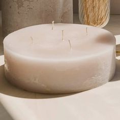 a white candle sitting on top of a table next to a vase with straws