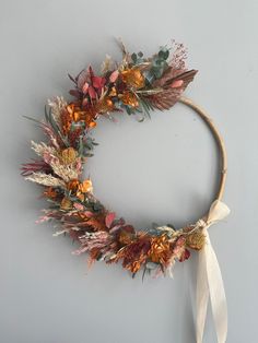 a wreath made out of dried flowers and leaves with a white ribbon hanging on the wall