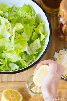 someone is peeling an orange slice into a bowl of lettuce and lemons