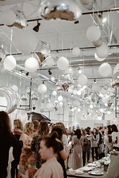 a large group of people standing in a room filled with white and silver balls hanging from the ceiling