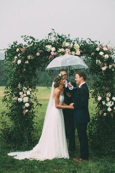 a bride and groom standing under an umbrella in front of a floral arch at their wedding