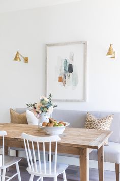 a dining room table with white chairs and a bowl of fruit on it