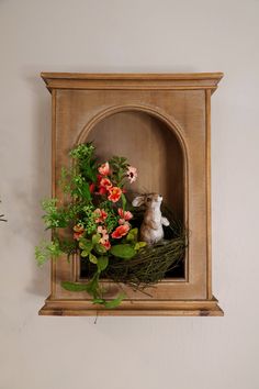 a rabbit sitting on top of a wooden shelf with flowers and greenery in front of it