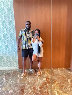 a man and woman taking a selfie in front of a wall with an umbrella