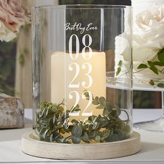 a candle is sitting in a glass container with greenery on the table next to it