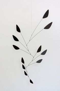 a metal wind chime with black leaves hanging from it's center point on a white wall