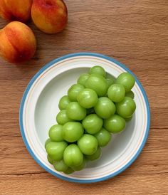 a plate with green grapes on it next to some peaches and two apricots