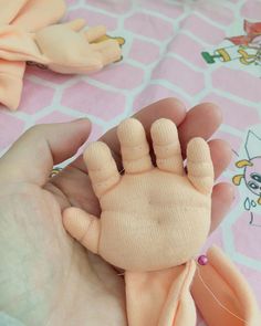 a person holding a small doll in their hand on a pink blanket with other dolls