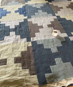 a bed with a blue and brown quilt on it's side, next to a cup