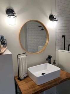 a white sink sitting under a round mirror on top of a wooden counter next to a bath tub