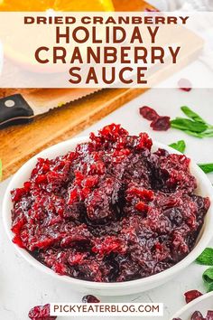 cranberry sauce in a white bowl on a cutting board with oranges and leaves