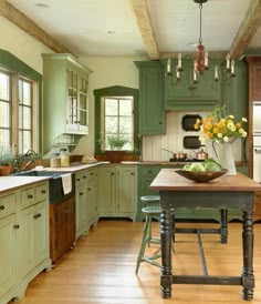 a large kitchen with green cabinets and wooden flooring is pictured in this image, the island has a bowl of fruit on it