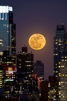 the full moon is seen over skyscrapers in new york city