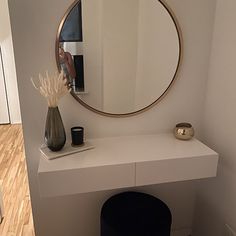 a white table with a round mirror and vase on it next to a black stool