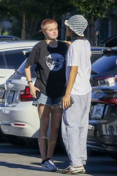 two people standing next to each other in front of parked cars and looking at each other