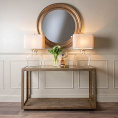 a table with a vase and flowers on it in front of a round mirror above