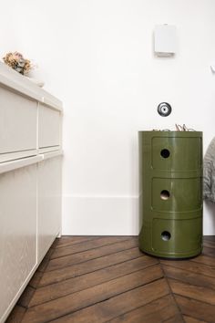 a green cabinet sitting next to a bed in a room with white walls and wooden floors