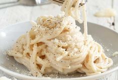 a fork is lifting up some pasta from a white bowl