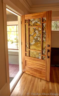 an open wooden door with flowers on the glass and wood frame, in front of a window