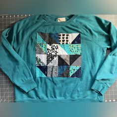 A Thrifted Crewneck Sweater, In Teal, Size Xlarge. Custom Made Quilt Square On The Center Front Of Jumper. Various Fun Fabrics, And One Featuring A Cute Cat! Stand Out In Style, In A Sustainable And Unique Way! Measurements In Photos: Total Length 23.5 Inches, Pit To Pit 24 Inches. Casual Raglan Sleeve Tops With Patchwork, Quilt Applique Sweatshirt, Thrifted Crewneck, Cat Stand, Fur Lined Hoodie, Quilted Sweater, Fuzzy Hoodie, Applique Sweatshirt, Stitch Hoodie