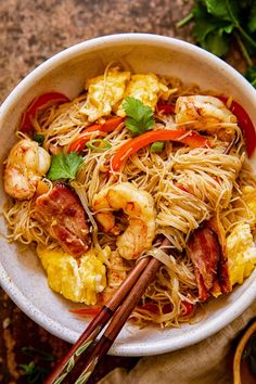 a white bowl filled with noodles and shrimp on top of a table next to chopsticks