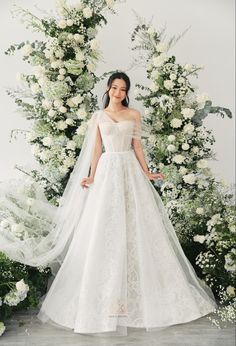 a woman in a white wedding dress standing next to a flower covered arch with flowers