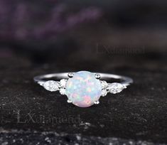 a white opal and diamond ring sitting on top of a rock