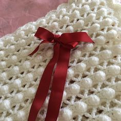 a white crocheted blanket with a red ribbon