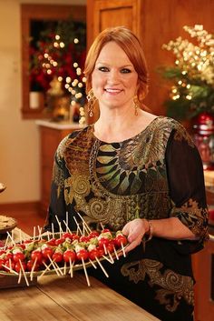 a woman standing in front of a wooden table holding a tray with toothpicks on it