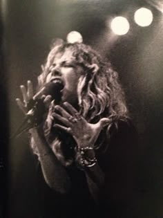 a black and white photo of a woman holding her hands up to her face while singing into a microphone