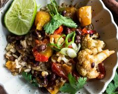 a white bowl filled with rice and vegetables next to lime wedges on top of a wooden table