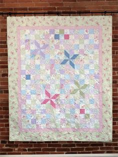 a pink and blue quilt hanging on a brick wall