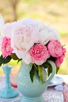 pink and white flowers in a blue vase on a lace tablecloth with other items