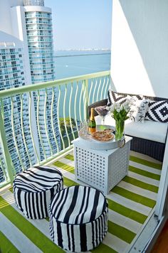 a balcony with green and white striped rugs, two stools and a coffee table