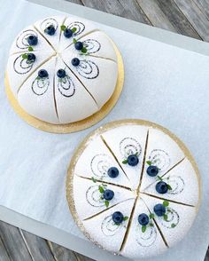 two white cakes with blueberries on them sitting on top of a piece of paper