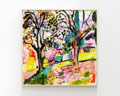 a painting hanging on the wall in front of a white wall with trees and grass