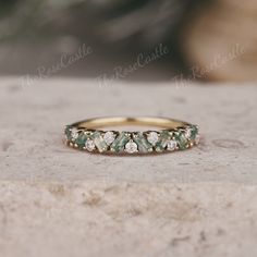 a gold ring with green and white stones on it sitting on top of a rock