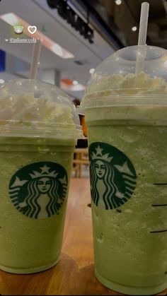 two starbucks drinks sitting next to each other on top of a wooden table in a restaurant