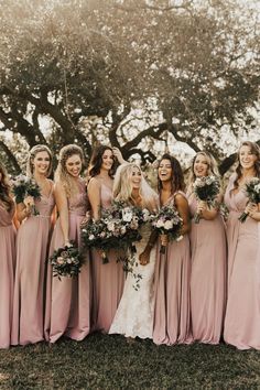 a group of women standing next to each other in front of trees and holding bouquets