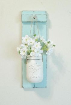 a mason jar with flowers in it hanging from a wall mounted shelf on the wall