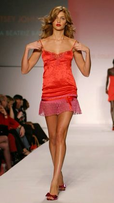 a woman is walking down the runway in a red dress and high heeled shoes