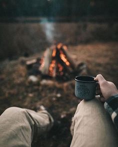 someone holding a coffee cup in front of a campfire